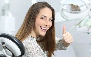 Smiling woman in dental chair with thumbs up
